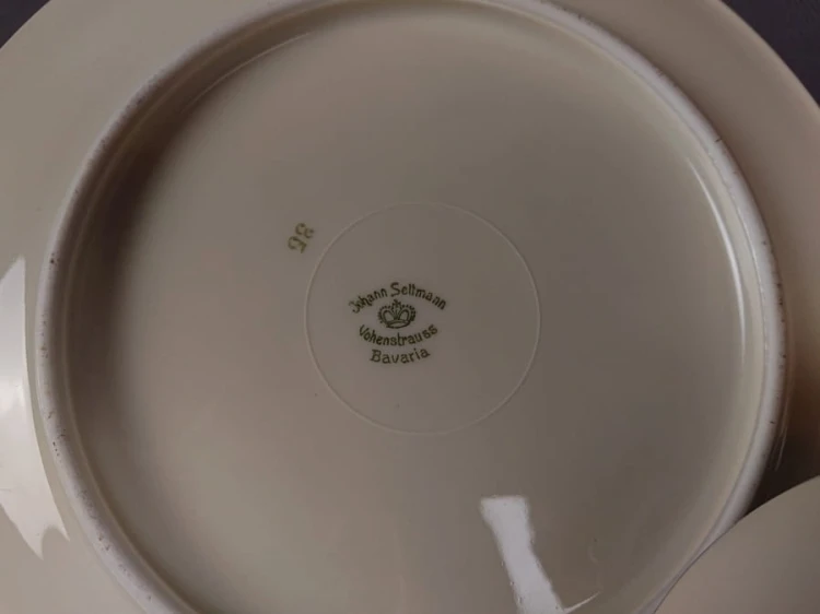 Zestaw niemieckiej firmy Johann Seltmann z lat 40. XX w. składa się z filiżanki, małego spodka i talerzyka deserowego. Wykonany z kremowej porcelany. Wnętrze filiżanki i ranty talerzy zdobią delikatne girlandy kwiatów w odcieniach lila, różu i błękitu.