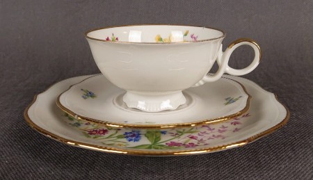 Porcelanowy zestaw śniadaniowy niemieckiej fabryki Oscar Schaller z lat 40 - 50. XX w. składa się z filiżanki na stopce, spodka i talerza śniadaniowego. Każdy element formowany jest z delikatnie kremowej porcelany o lekko perłowym połysku.