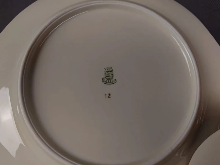 Porcelanowy zestaw śniadaniowy niemieckiej fabryki Porzellanfabrik Lettin – Heinrich Baensch pochodzi z lat powojennych (lata 50. XX w.). W skład kompletu wchodzi filiżanka na stopce, spodek i talerz śniadaniowy, wszystkie wykonane z delikatnie kremowej.