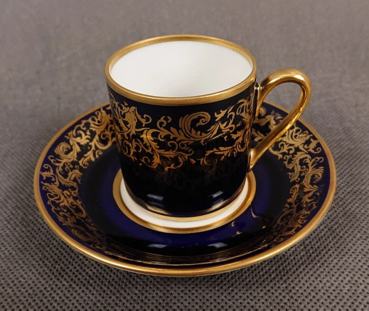 Filiżanka ze spodkiem do kawy espresso, pochodzi z drugiej połowy XX. wieku. Zestaw wykonany z wyjątkowo delikatnej dobrej jakości cienkiej białej porcelany.  Filiżanka i spodek dekorowana kobaltem a na tym tle złote dekoracja.