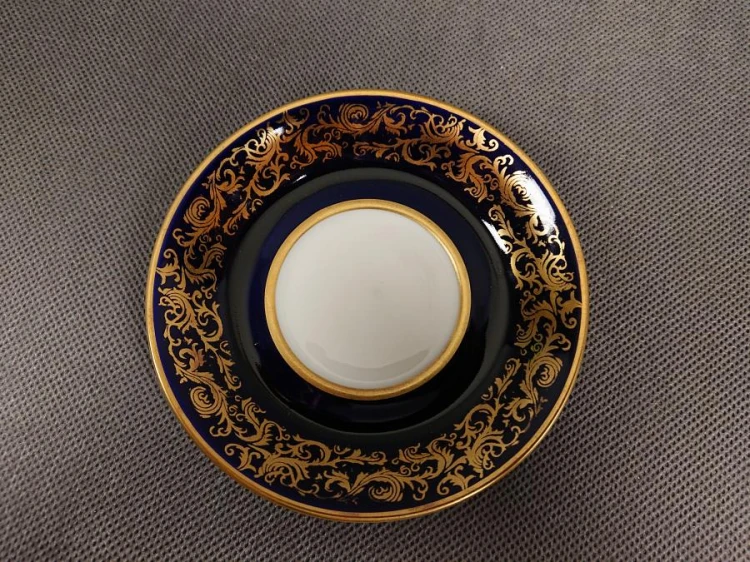 Filiżanka ze spodkiem do kawy espresso, pochodzi z drugiej połowy XX. wieku. Zestaw wykonany z wyjątkowo delikatnej dobrej jakości cienkiej białej porcelany.  Filiżanka i spodek dekorowana kobaltem a na tym tle złote dekoracja.