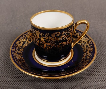 Filiżanka ze spodkiem do kawy espresso, pochodzi z drugiej połowy XX. wieku. Zestaw wykonany z wyjątkowo delikatnej dobrej jakości cienkiej białej porcelany.  Filiżanka i spodek dekorowana kobaltem a na tym tle złote dekoracja.