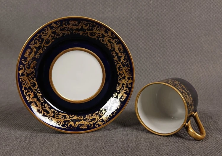 Filiżanka ze spodkiem do kawy espresso, pochodzi z drugiej połowy XX. wieku. Zestaw wykonany z wyjątkowo delikatnej dobrej jakości cienkiej białej porcelany.  Filiżanka i spodek dekorowana kobaltem a na tym tle złote dekoracja.