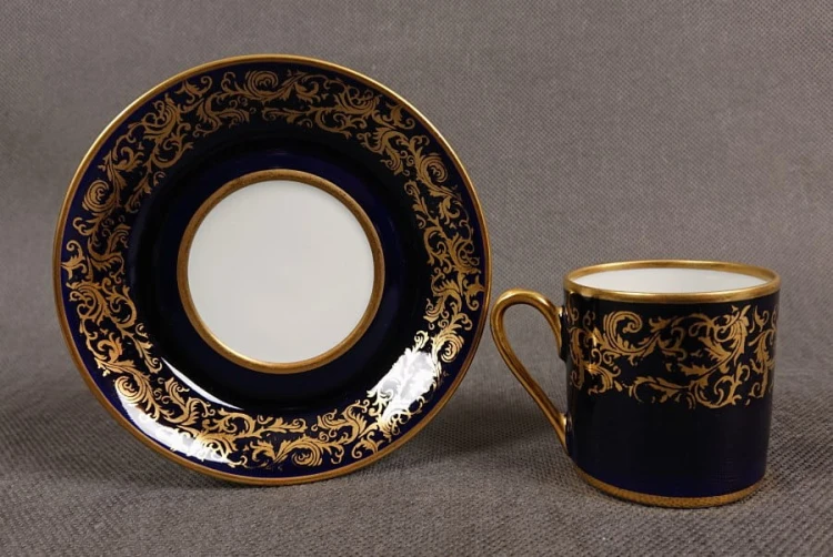 Filiżanka ze spodkiem do kawy espresso, pochodzi z drugiej połowy XX. wieku. Zestaw wykonany z wyjątkowo delikatnej dobrej jakości cienkiej białej porcelany.  Filiżanka i spodek dekorowana kobaltem a na tym tle złote dekoracja.