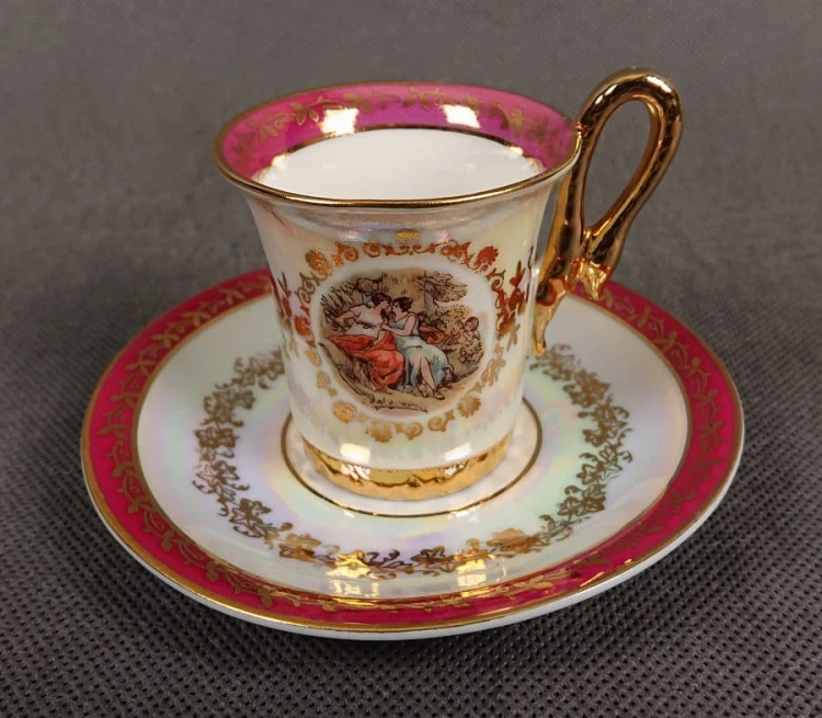 Espresso filiżanka ze scenką Martinroda Fridrich. Porcelanowa filiżanka ze spodkiem do espresso, wyprodukowana w niemieckiej fabryce porcelany Martinroda, prezentuje wyrafinowany styl rokoko, charakteryzuje się bogatym zdobieniami i perłowym połyskiem.