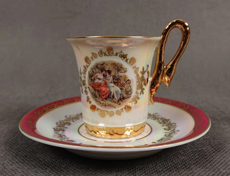 Espresso filiżanka ze scenką Martinroda Fridrich. Porcelanowa filiżanka ze spodkiem do espresso, wyprodukowana w niemieckiej fabryce porcelany Martinroda, prezentuje wyrafinowany styl rokoko, charakteryzuje się bogatym zdobieniami i perłowym połyskiem.