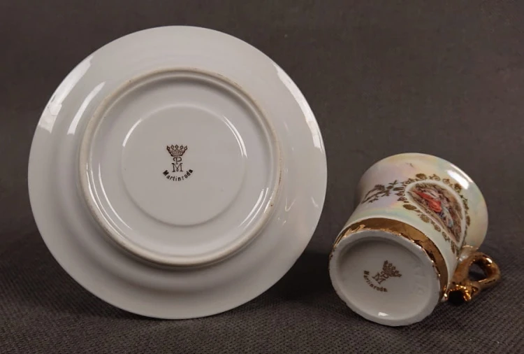 Espresso filiżanka ze scenką Martinroda Fridrich. Porcelanowa filiżanka ze spodkiem do espresso, wyprodukowana w niemieckiej fabryce porcelany Martinroda, prezentuje wyrafinowany styl rokoko, charakteryzuje się bogatym zdobieniami i perłowym połyskiem.