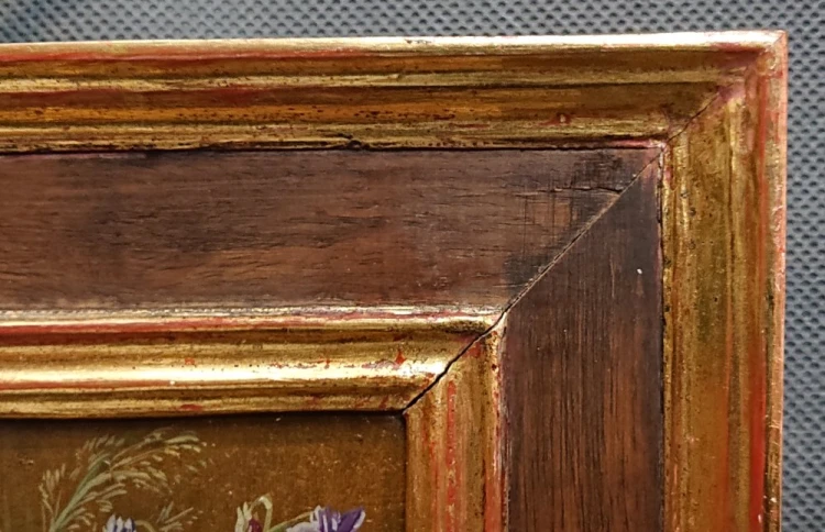 Artystyczne zbliżenie na rzeźbiony narożnik złotej ramy i fragment martwej natury z kwiatami.