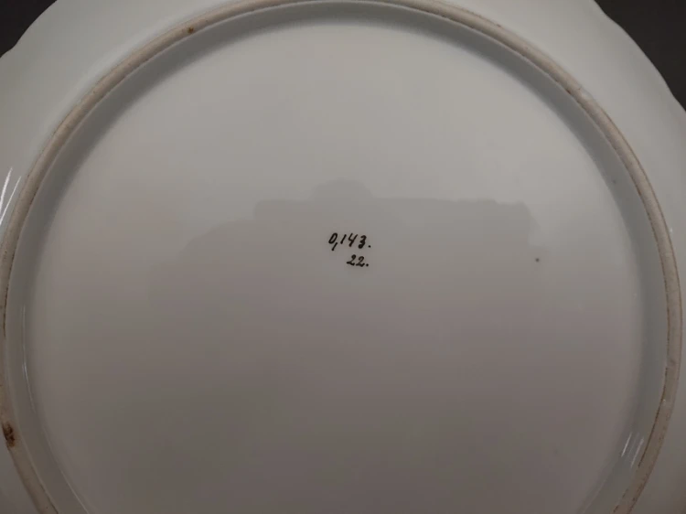 Zbliżenie na spód porcelanowej patery z odręcznie napisanym numerem 0,143 oraz 22