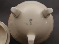 Zbliżenie na dno bomboniery prezentujące zieloną koronę, monogram manufaktury August Schweig oraz wybity numer 28
