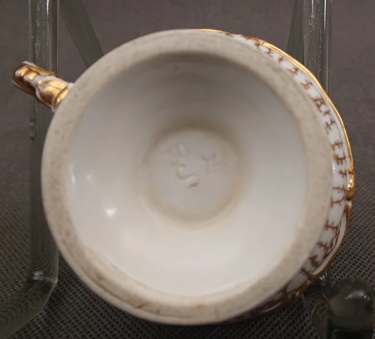 Spód porcelanowej podstawy antycznej filiżanki z wyraźnie wyciśniętą w masie literą S oraz numerami