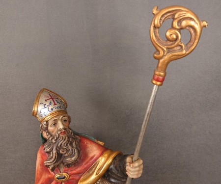 Górna połowa rzeźby Świętego Mikołaja z bliska ukazująca dłoń trzymającą srebrzysty kij pastorału ze złotym zwieńczeniem.