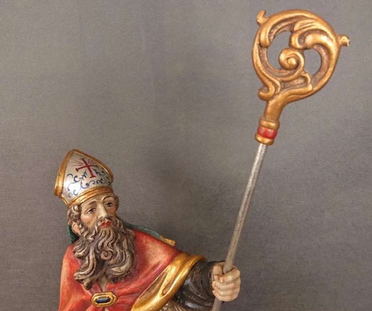 Górna połowa rzeźby Świętego Mikołaja z bliska ukazująca dłoń trzymającą srebrzysty kij pastorału ze złotym zwieńczeniem.