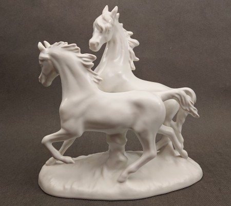 Porcelanowa figura białego, lśniącego konia marki Goebel na jasnym tle, ujęcie z profilu eksponujące sylwetkę zwierzęcia.