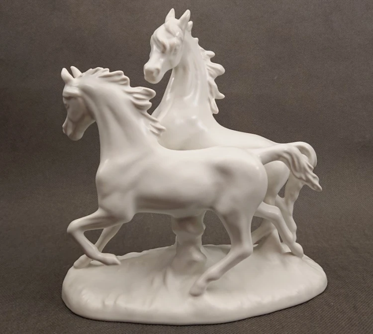 Porcelanowa figura białego, lśniącego konia marki Goebel na jasnym tle, ujęcie z profilu eksponujące sylwetkę zwierzęcia.