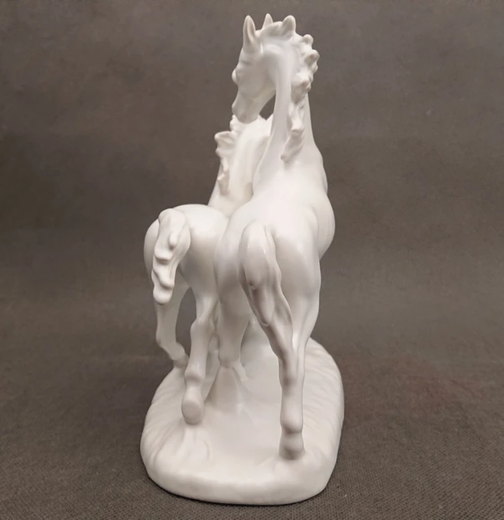 Porcelanowa figura białego, lśniącego konia marki Goebel na jasnym tle, ujęcie z tyłu ukazujące sylwetkę konia.