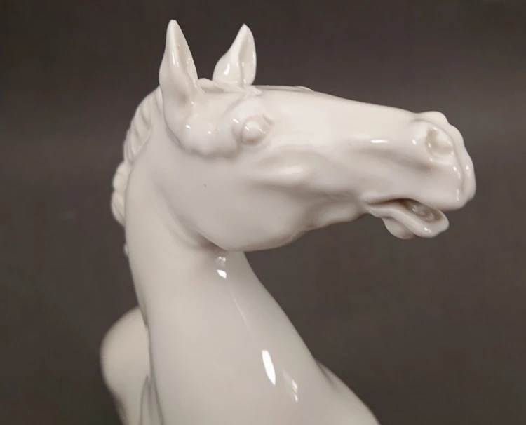 Zbliżenie na głowę porcelanowego konia wierzchowca, ukazujące precyzyjnie wymodelowany pysk, oczy oraz głęboki połysk białego szkliwa.