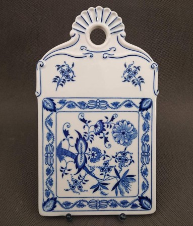 Widok naprzód porcelanowej deski z faliście wyciętym, ozdobnym uchwytem i okrągłym otworem do zawieszenia, zdobioną dwoma symetrycznymi bukietami kwiatów.