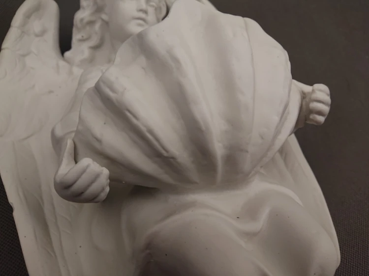 Kadr od dołu ukazujący spód i profil głębokiej misy w kształcie falowanej muszli trzymanej przez porcelanowego anioła.