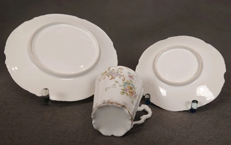 Odwrotna strona spodka, talerzyka deserowego i leżącej filiżanki, ukazująca nieszkliwione pierścienie podstawy oraz gładką, białą porcelanę.