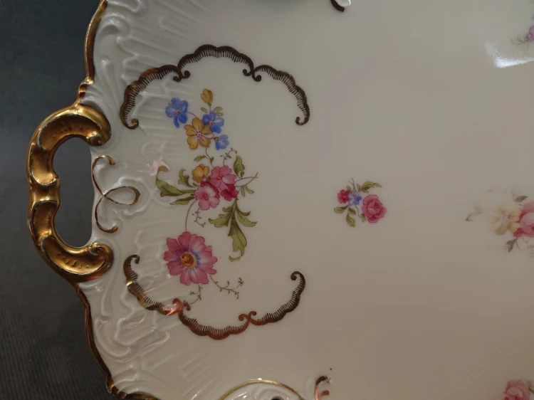 Detal malatury kwiatowej ujętej w złoconą ramkę na porcelanie w kolorze kości słoniowej